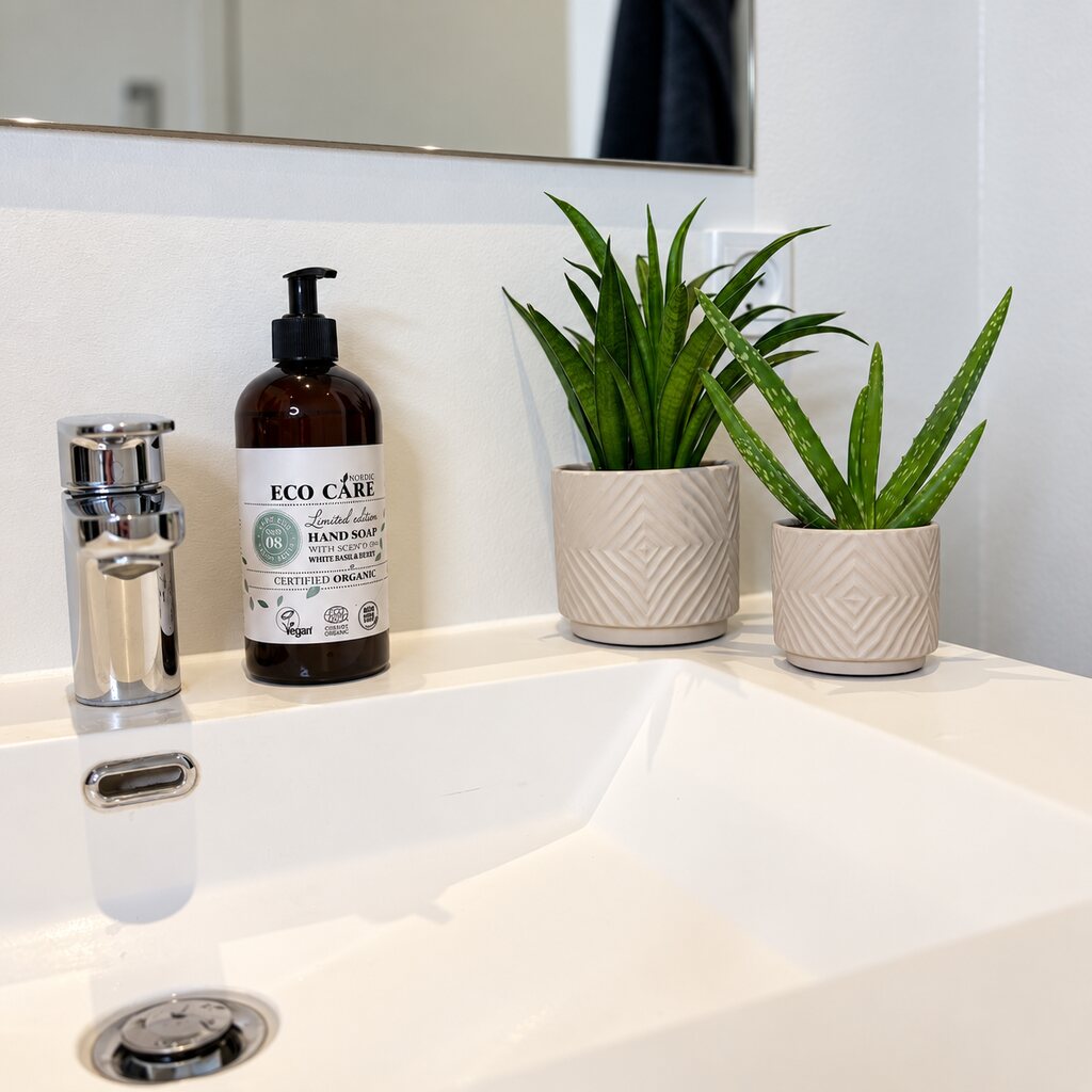 Sansevieria Panthera i lys mønstret krukke sammen med Aloe ved en hvid håndvask.