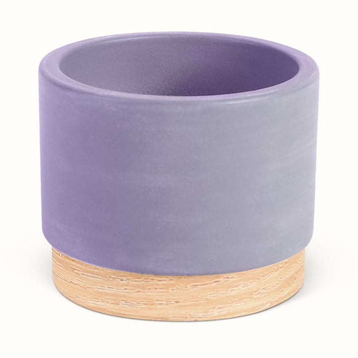En lyslilla potteskjuler i keramik med træbund